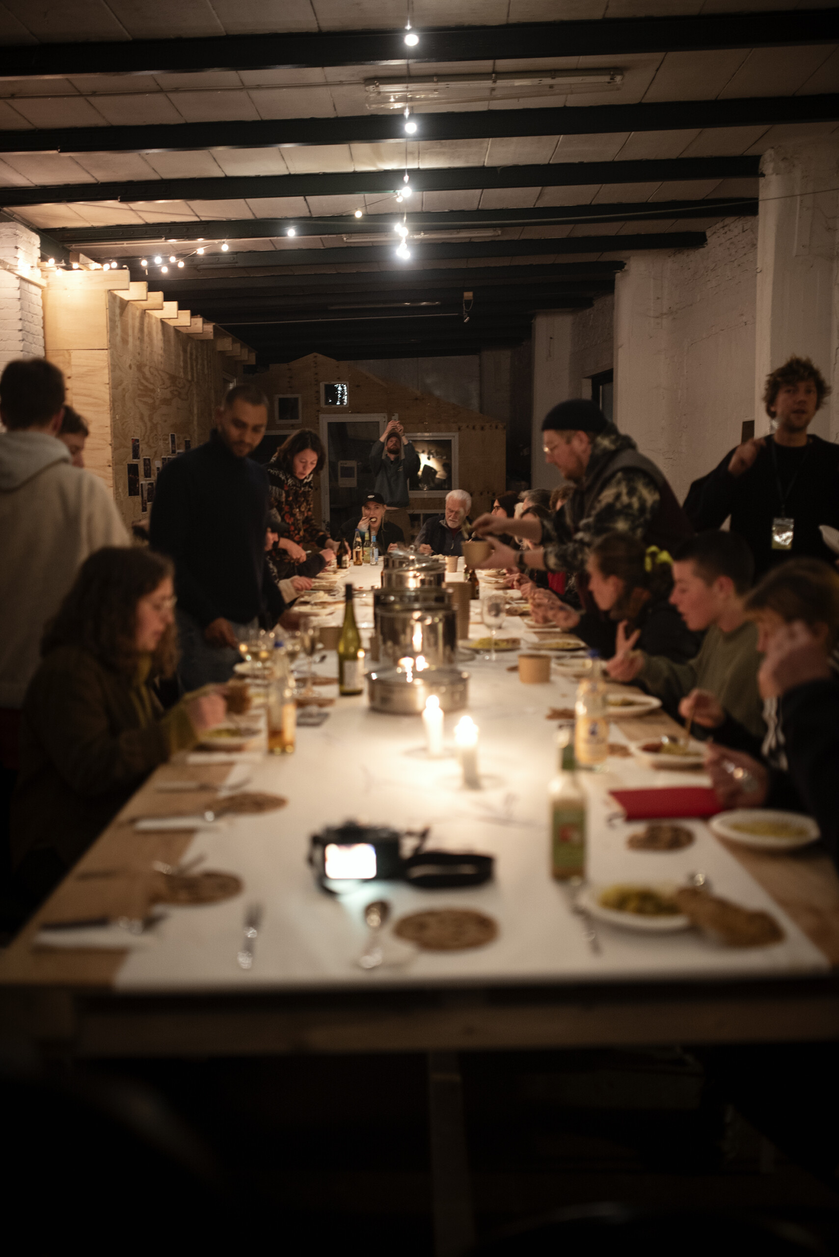 Menschen sitzen an einer langen Tafel im Kerzenschein und essen gemeinsam